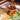 The Chocolate Tarts Masterclass features chocolate tarts with rich fillings, presented on a wooden stand alongside pastries, brownies, and macarons on a vibrant tea table set with plates, forks, and glasses in the sunlight.