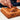 In the American Dessert Masterclass, someone decorates a square chocolate cake by hand with piped chocolate frosting and curved Maison Marou chocolate pieces on top for precise placement.