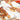 Someone decorates choux pastry eclairs with cream using a piping bag on a marble counter. Nearby, a tray of chocolate, cream, and sprinkle-topped eclairs awaits—perfect for the Pâte à Choux Masterclass.